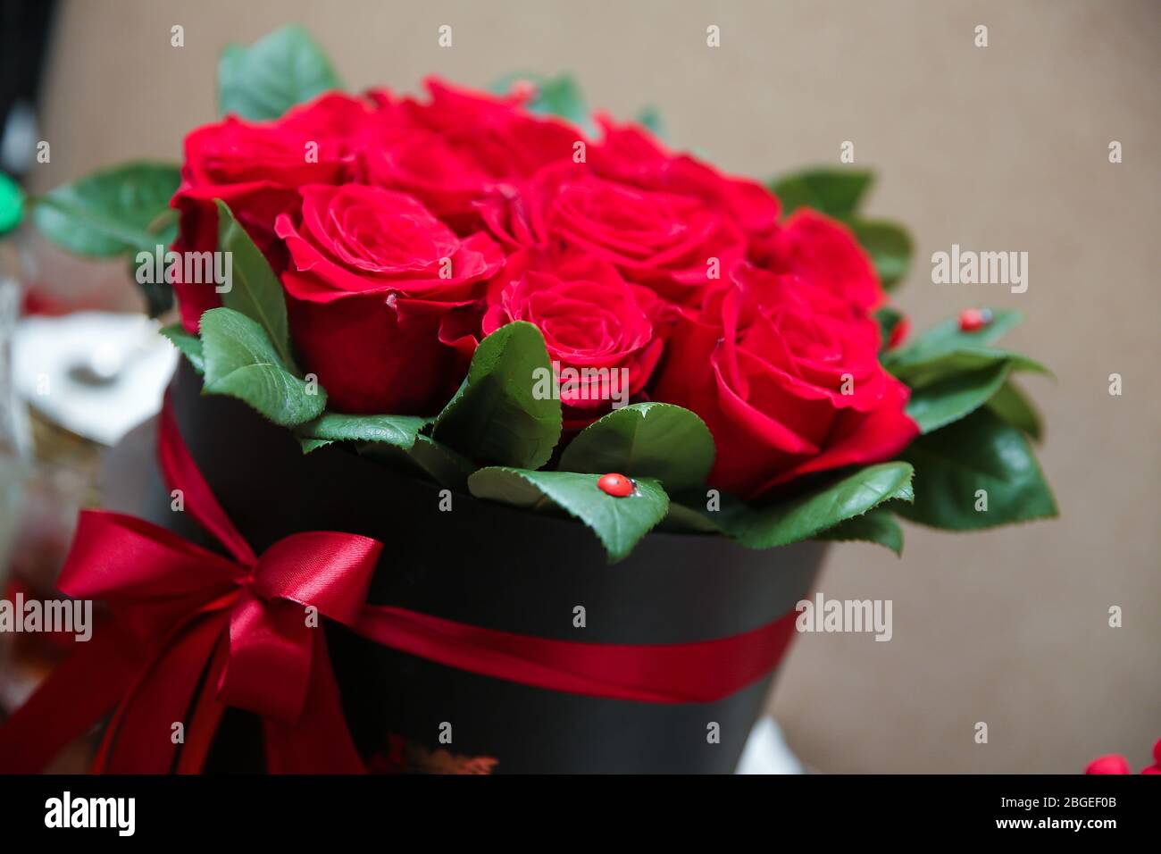 Un bouquet di rose rosse e bianche in una scatola rotonda rossa. Bouquet di fiori fatto di rose rosse, garofani rossi scuri, bacche nere e foglie verdi messo in Foto Stock