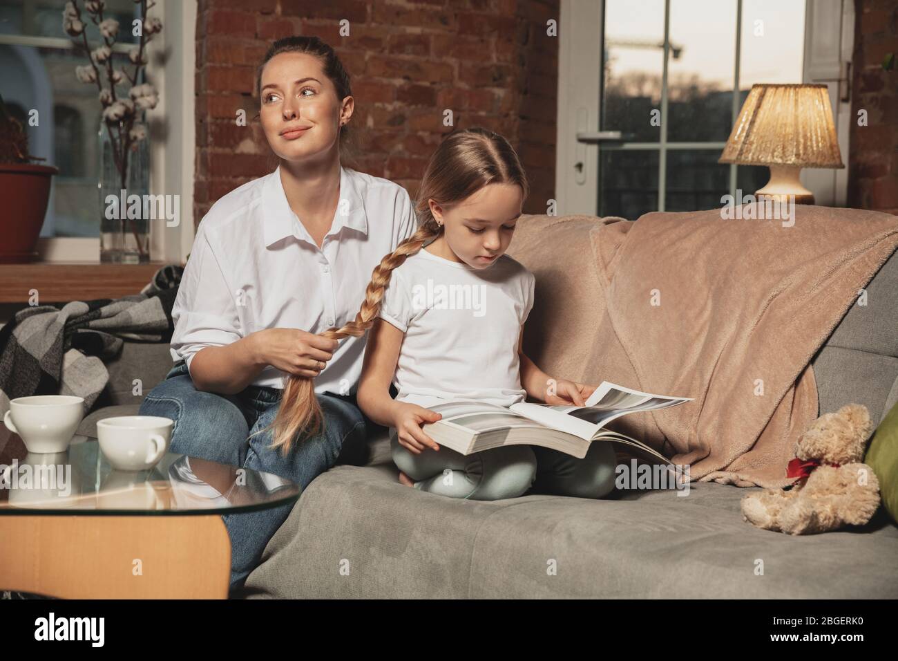 Acconciatura, acconciatura. Madre e figlia durante l'autoisolamento a casa mentre in quarantena, tempo di famiglia accogliente e comfort, vita domestica. Modelli allegri e felici sorridenti. Sicurezza, prevenzione, concetto di amore. Foto Stock