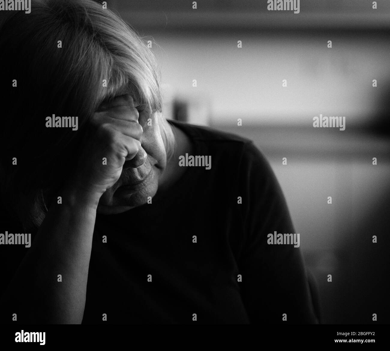 Donna depressa più anziana con la testa appoggiata su di lei hand.in un ambiente domestico. Foto Stock