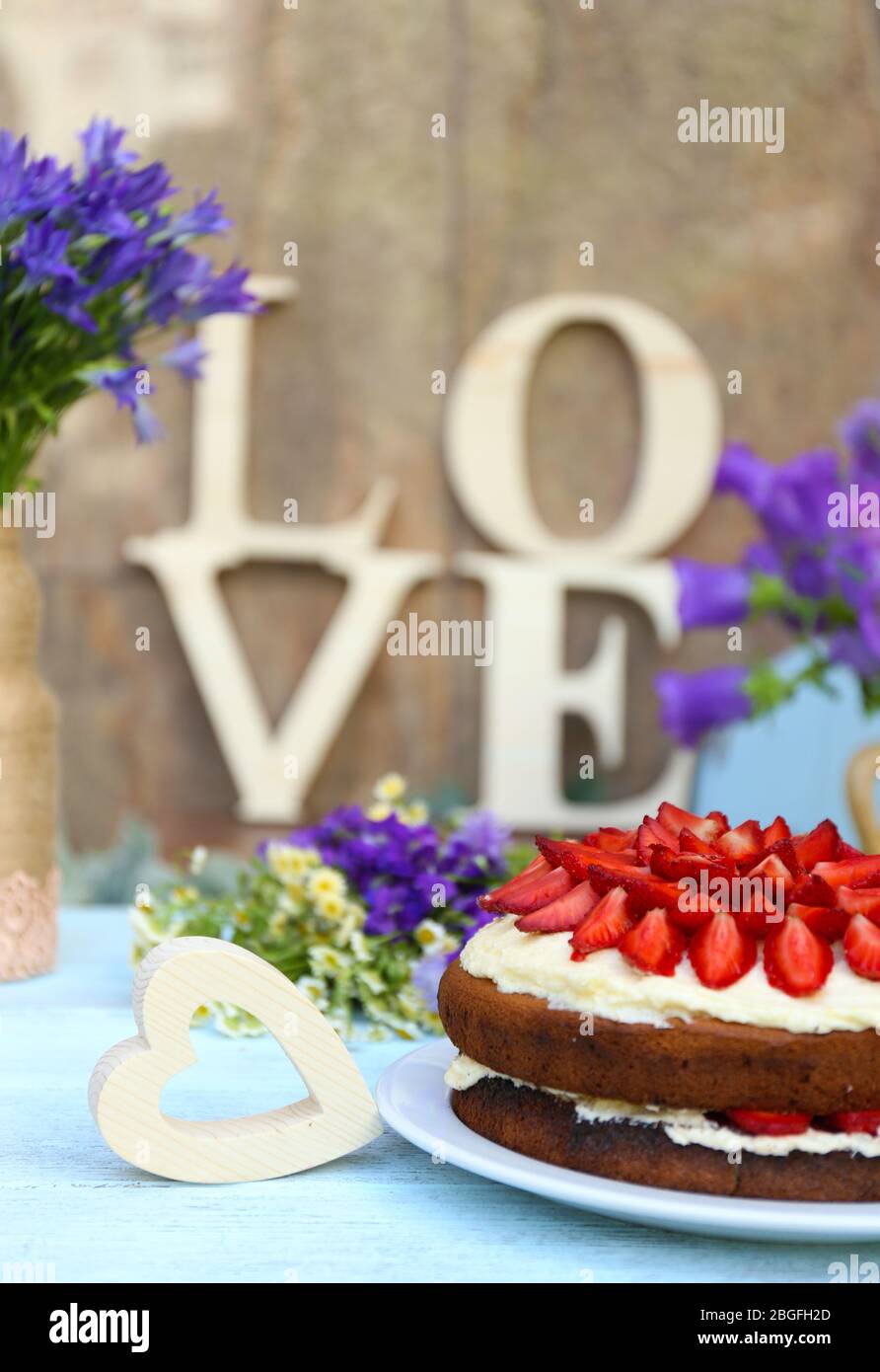Torta di fragole con fiori selvatici e lettere decorative a tavola Foto Stock