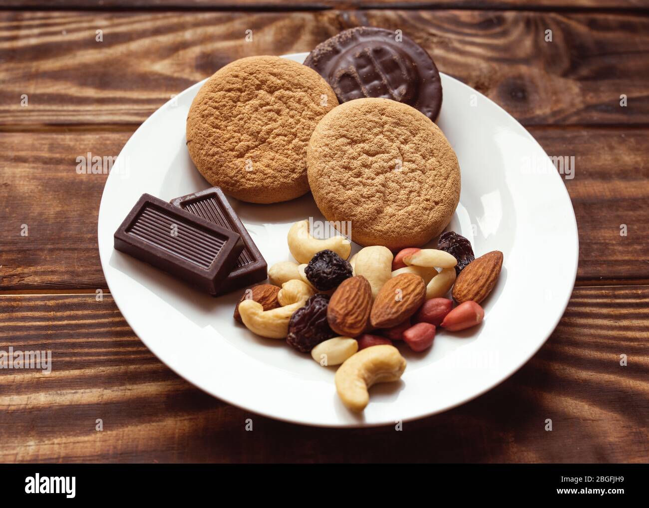 Tre torte, una varietà di noci e due cioccolatini sul piatto bianco su un tavolo di legno. Foto Stock