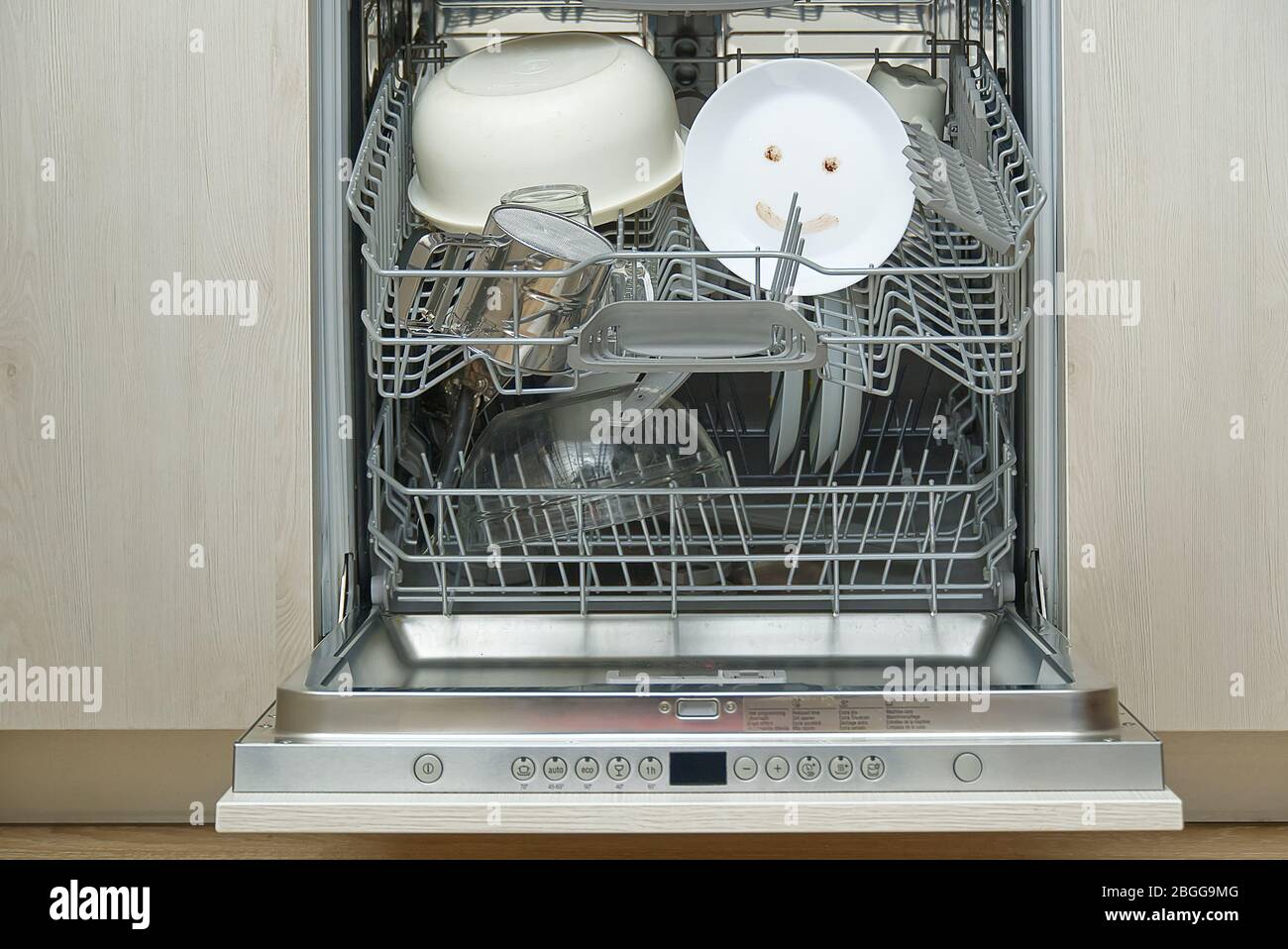 Piatti finemente lavati in lavastoviglie. Lavastoviglie integrata con piastre bianche davanti a vew e felice emozione sul piatto. Concetto di pulizia domestica semplice. Foto Stock