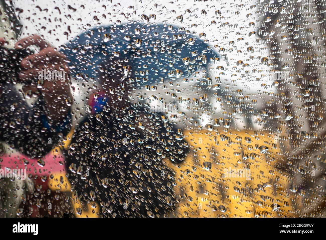 Pioggia sfocata in una finestra di vetro durante la pioggia, con ombrello sullo sfondo Foto Stock