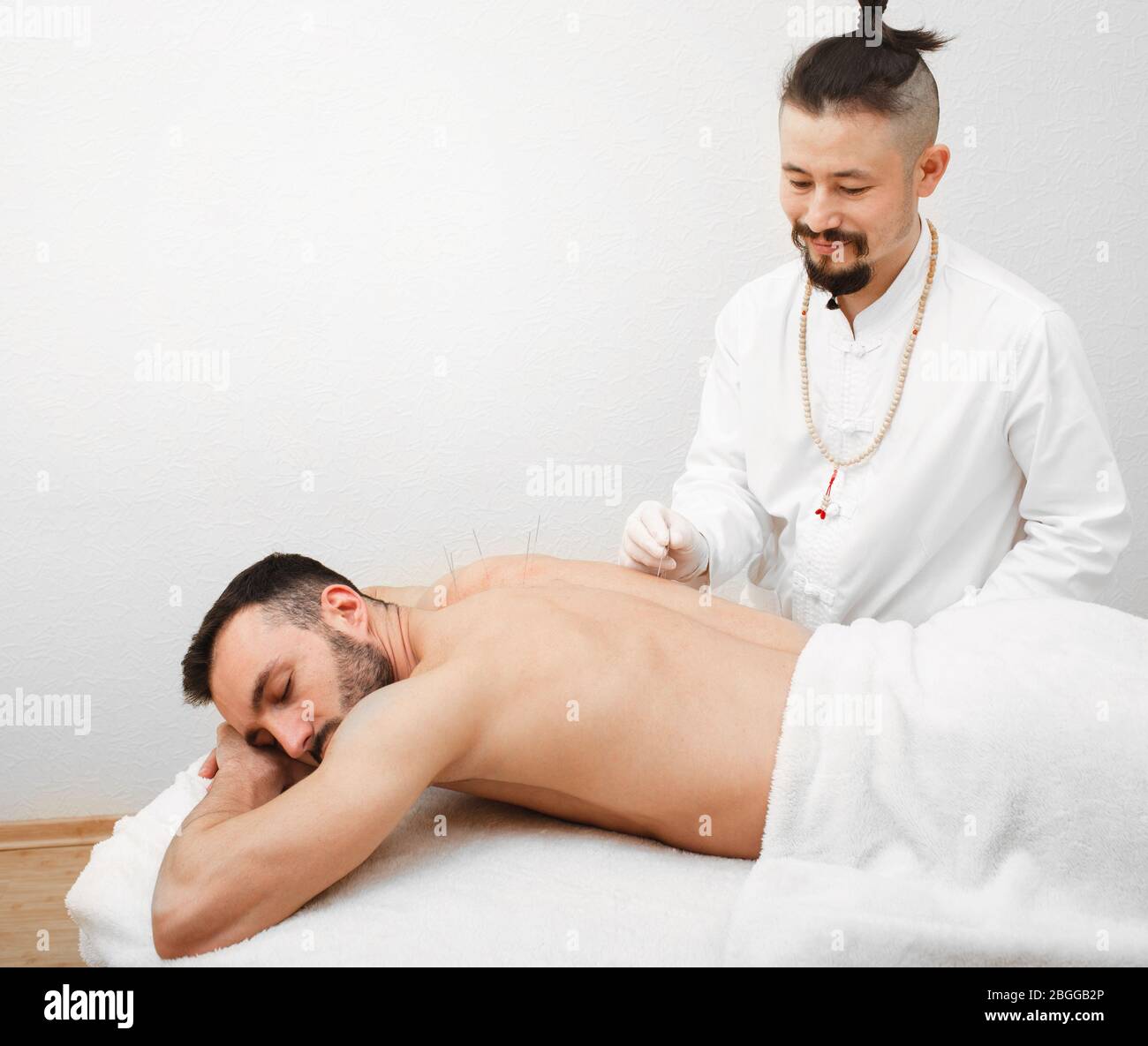 Riflessologo che fa una procedura di agopuntura per l'uomo con dolore alla schiena. Trattamento agopuntura della schiena. Procedura indolore Foto Stock
