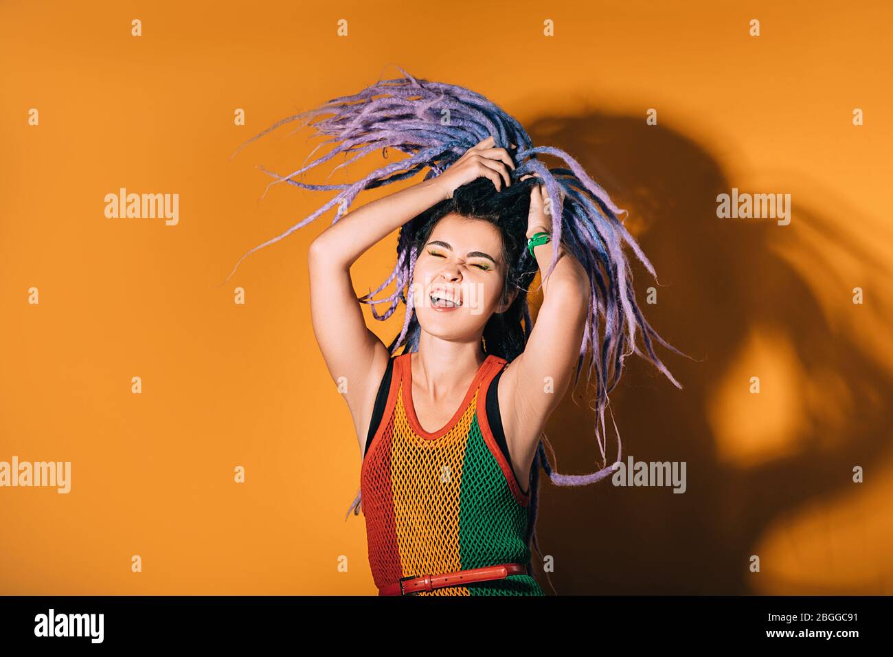 Donna con i Dreadlock viola sta ballando su uno sfondo arancione. La donna hipster ama la vita. Foto Stock