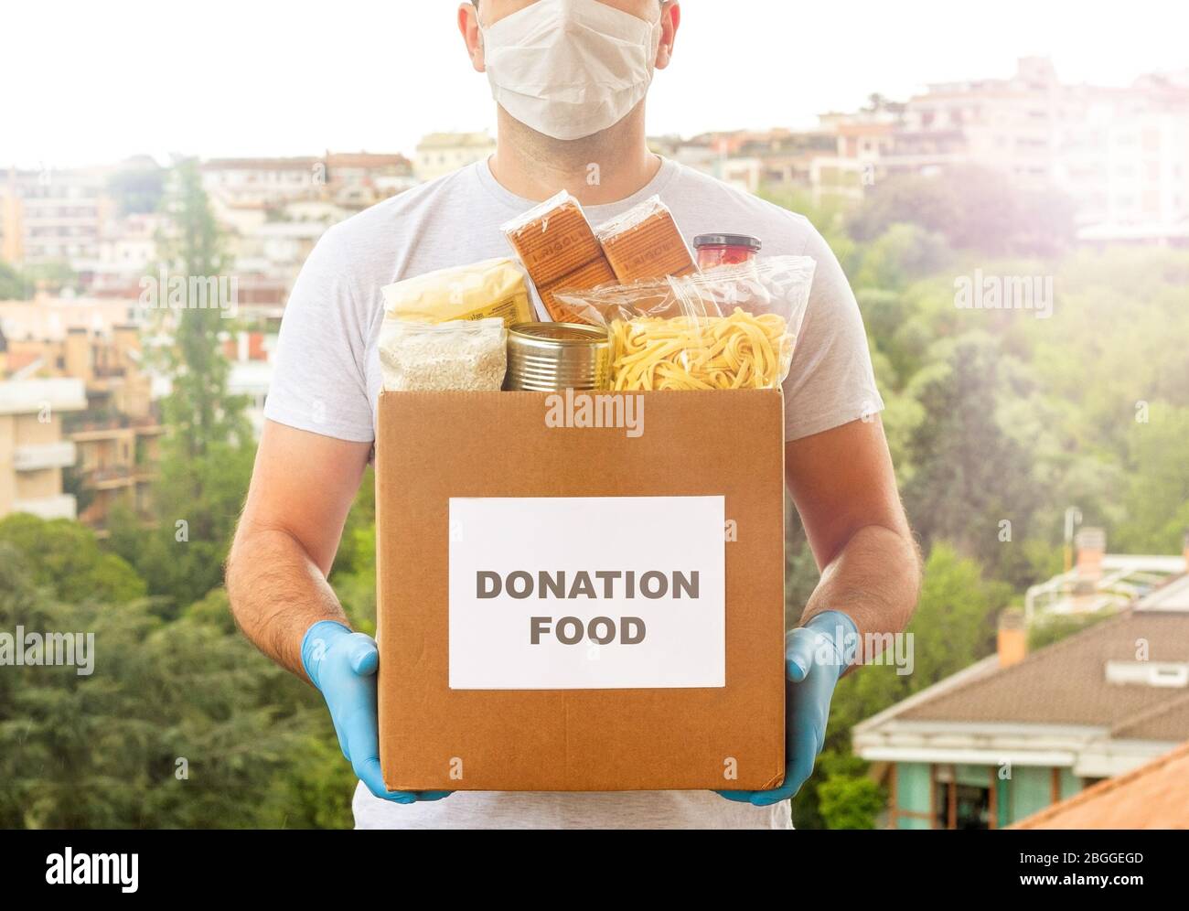 Scatola per la donazione. Consegna di cibo. Volontario. Aiuto alimentare. Un uomo in maschera e guanti medici tiene una scatola di cibo sulla strada Foto Stock