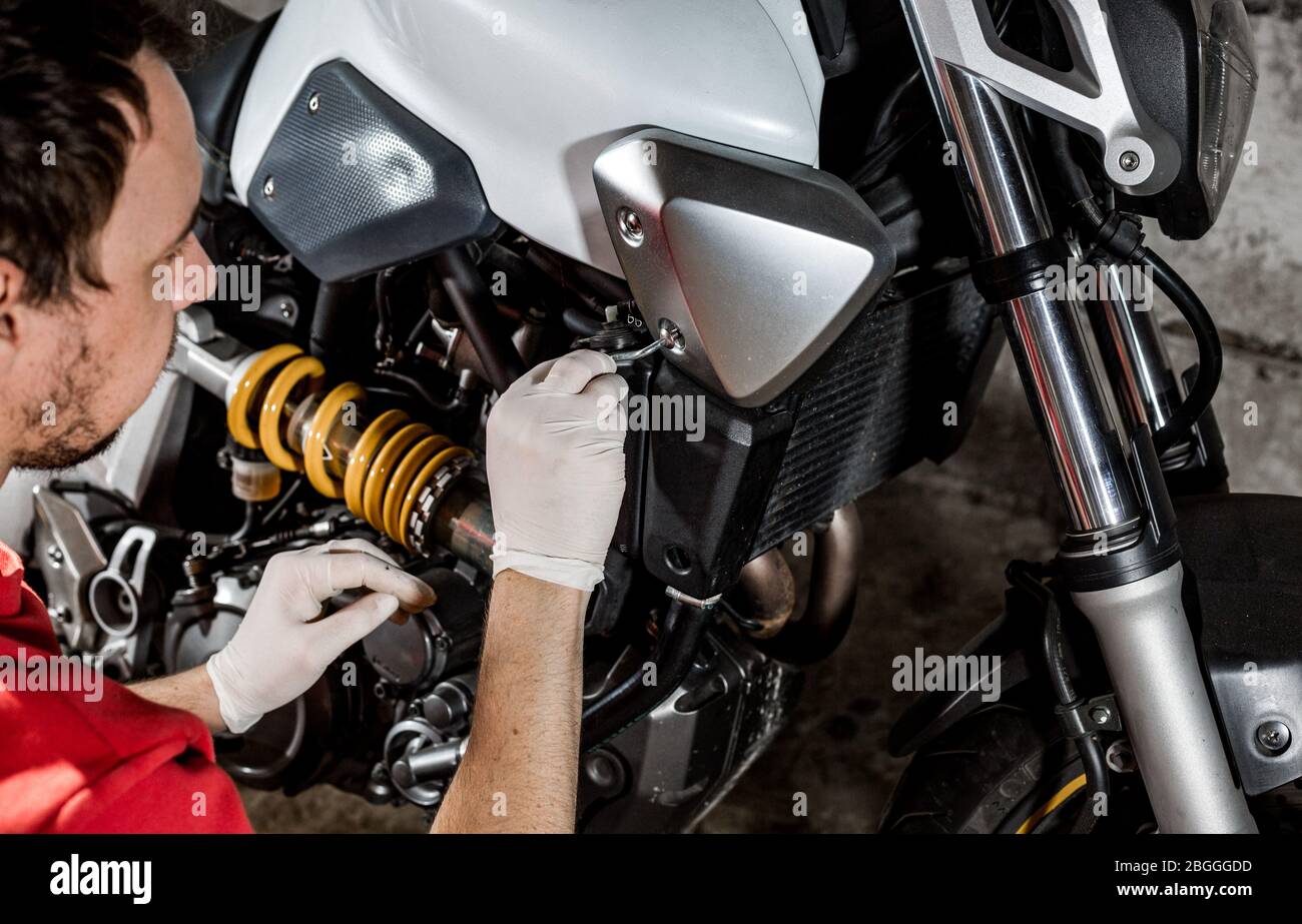 Riparatore meccanico che esegue la manutenzione o la riparazione, il fissaggio sulla motocicletta, moto, centro di assistenza Foto Stock