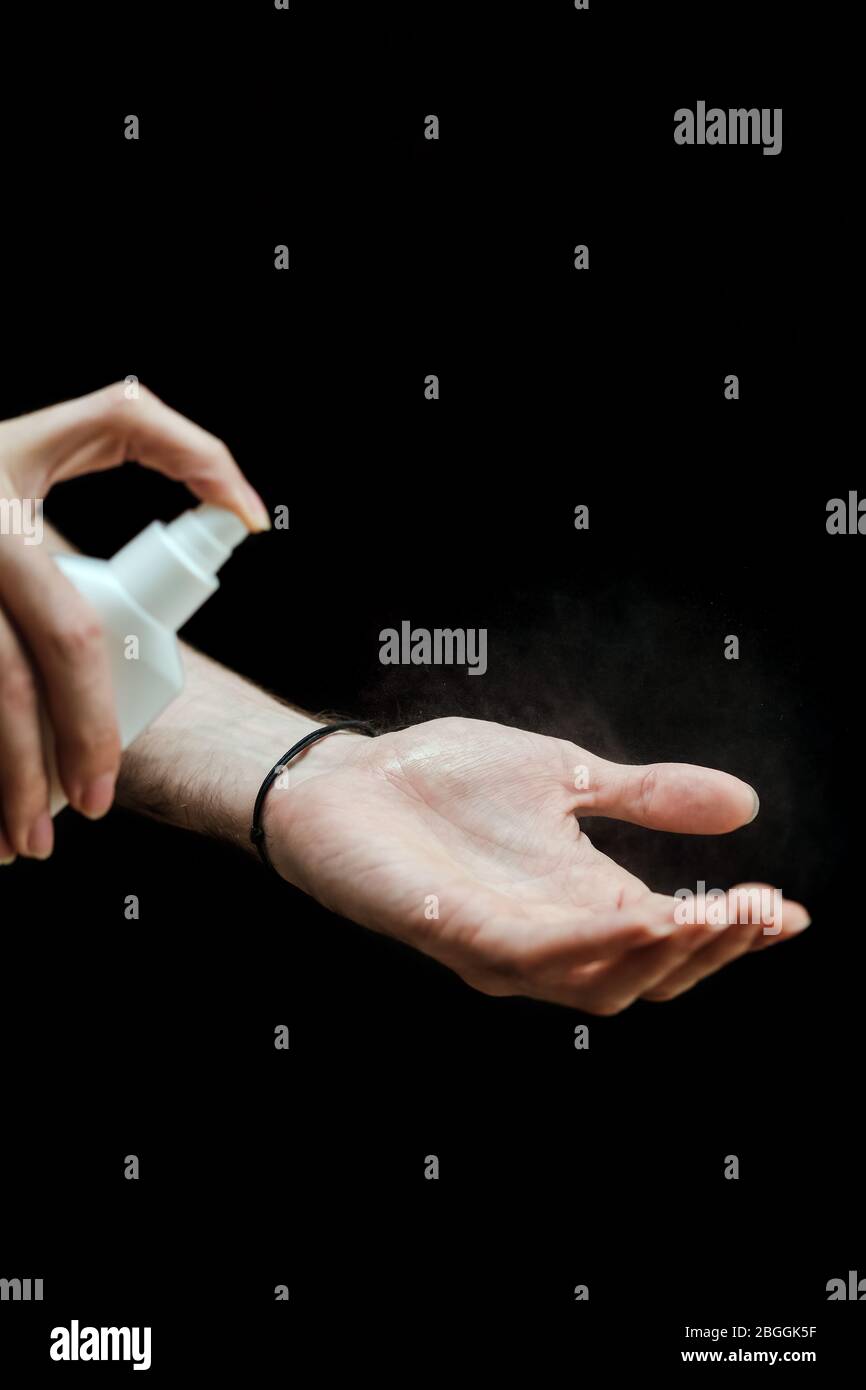 Mano maschile con uno spray disinfettante disinfettare la mano in casa su uno sfondo nero. Covid-19 quarantena di Coronavirus Pandemic. Isolamento a casa. P Foto Stock