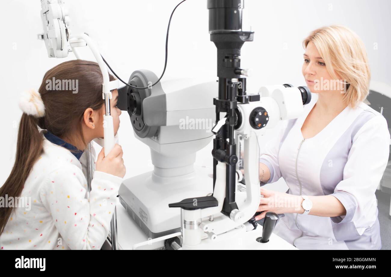 Medico femminile che guarda molto attentamente lo schermo del tonometro oftalmico per controllare correttamente la visione della ragazza. Esame visivo Foto Stock