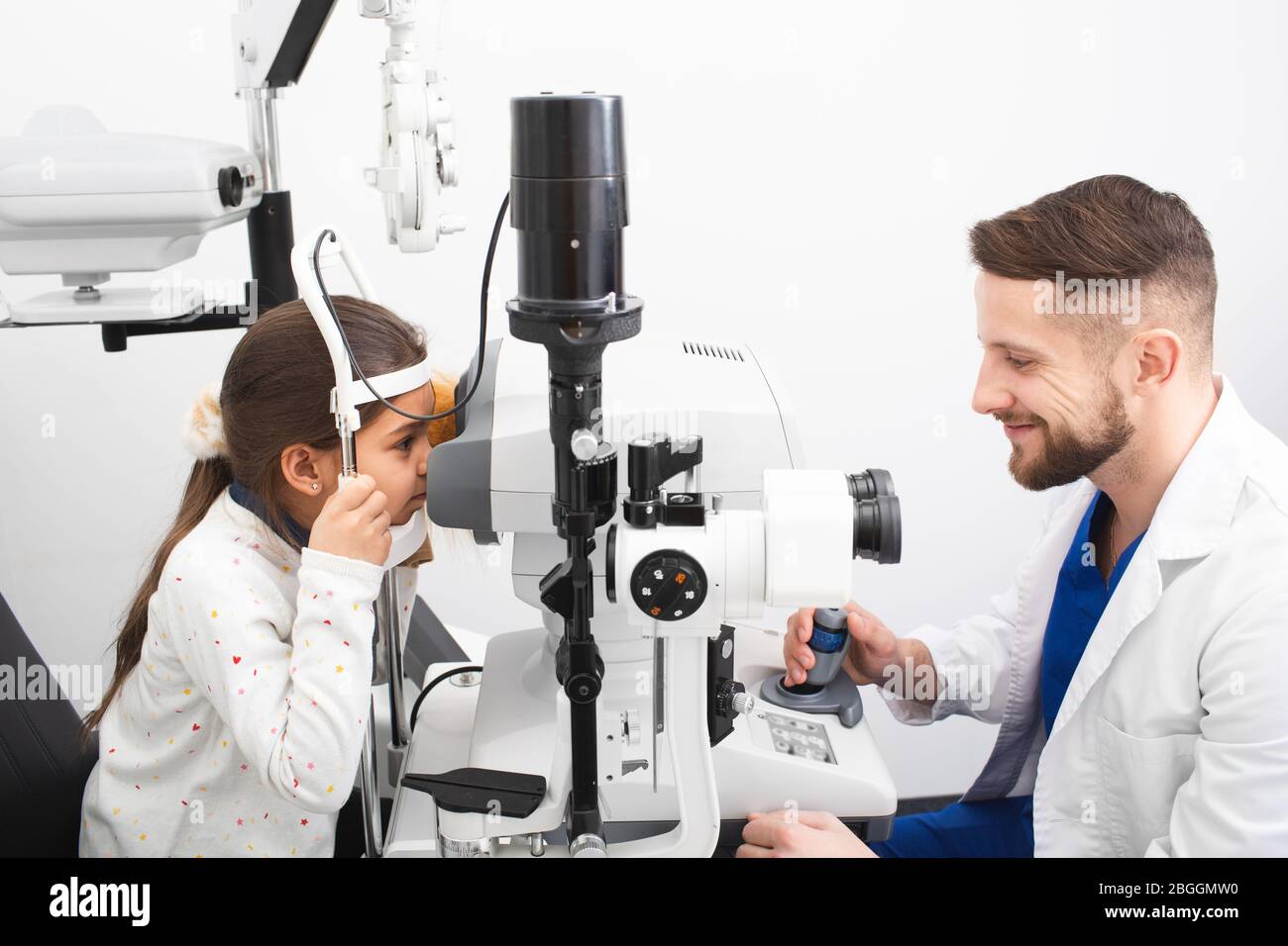 Il medico di sesso maschile controlla la vista di una ragazza su attrezzature moderne in clinica. Il tonometro misura la pressione oculare del paziente. Correzione della visione Foto Stock