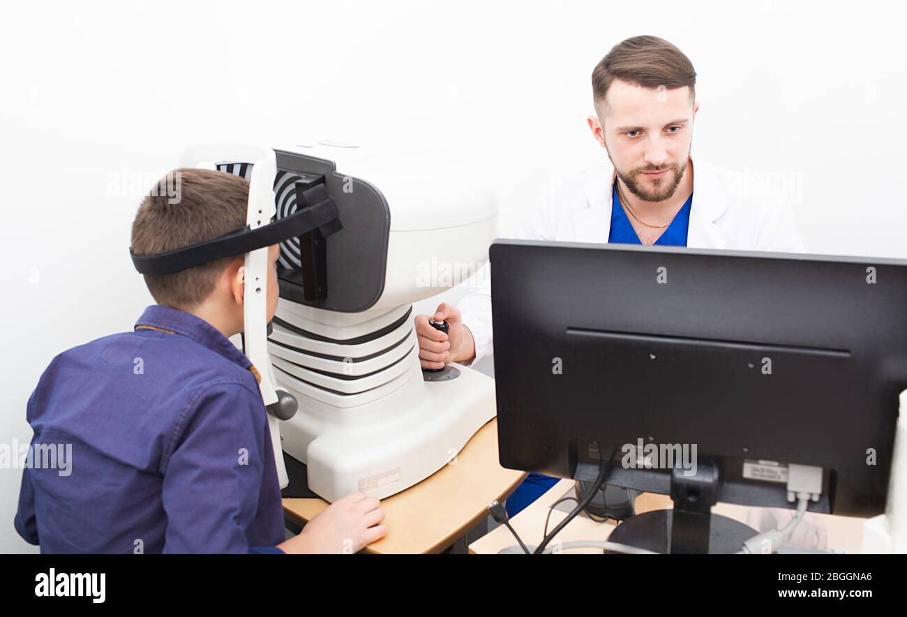 Il medico dell'optometristo controlla la vista del ragazzo dell'adolescenza. Misurazione delle pupille degli occhi e loro risposta alla luce Foto Stock