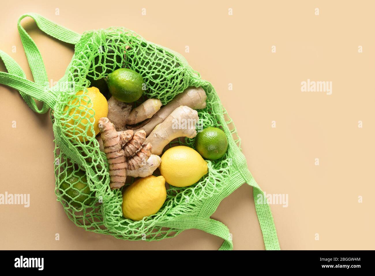 Sacco a rete verde con verdure, limone zenzero, altri alimenti su beige naturale. Zero sprechi. Cibi vegani sani. Stile di vita sostenibile. Vista dall'alto. Foto Stock