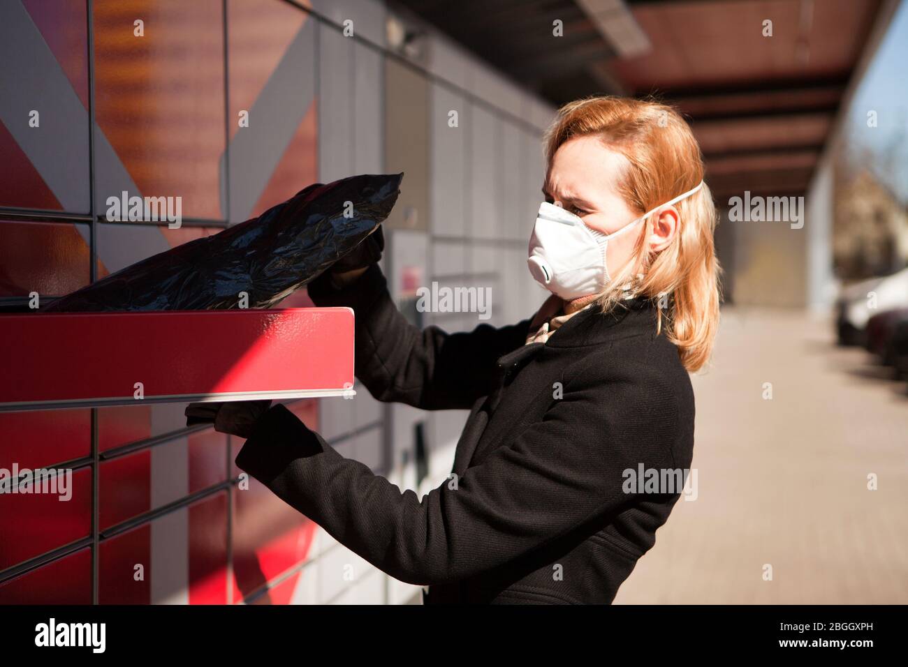 la signora che indossa una maschera facciale riceve un pacco o un pacco da un terminale postale a Tallinn. Donna che indossa una maschera respiratoria facciale - protezione da Foto Stock