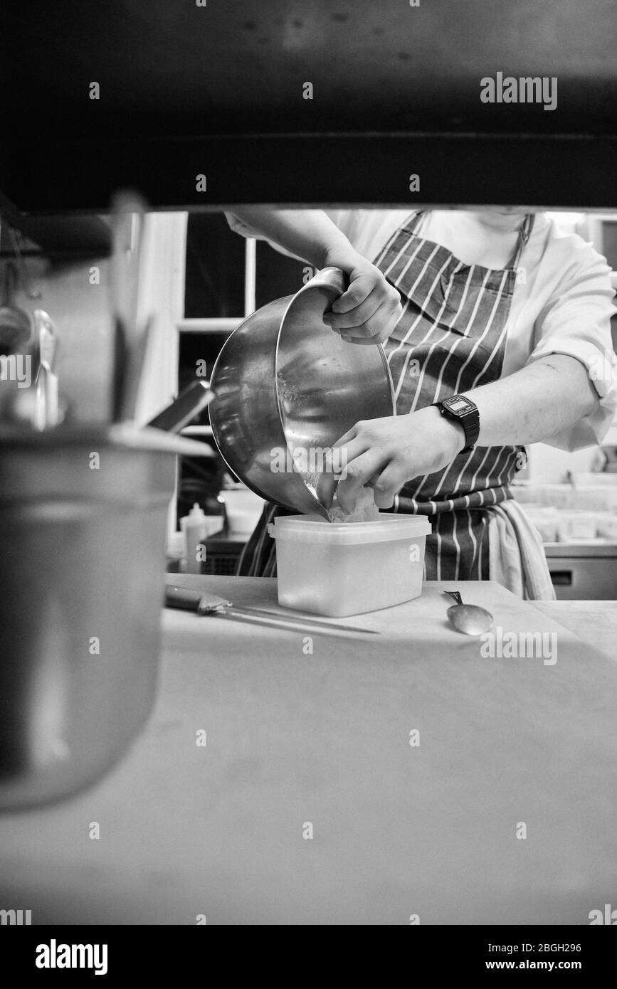 Chef che mette formaggio grattugiato in contenitore di plastica Foto Stock