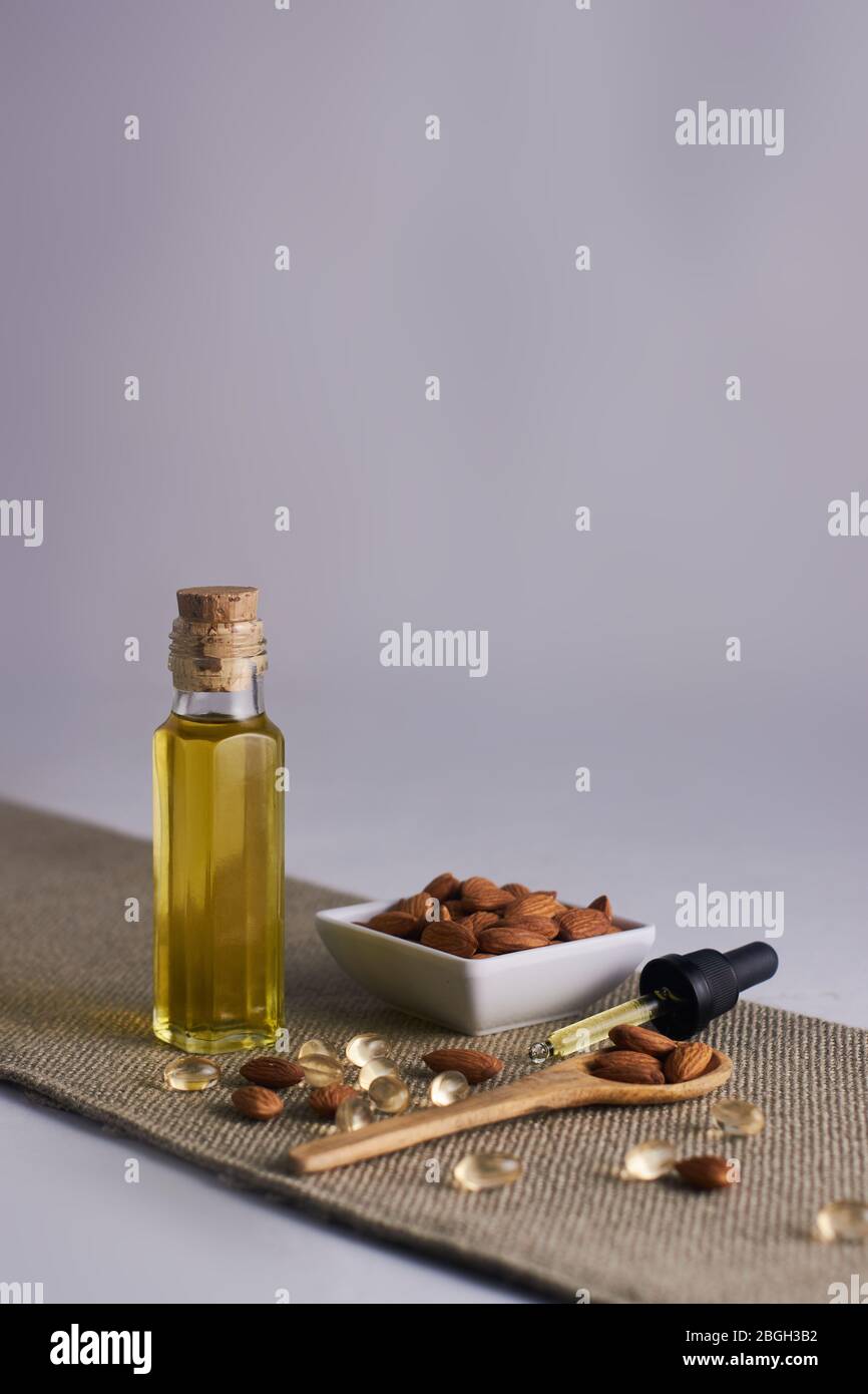 olio di mandorle in bottiglia di vetro con fondo bianco e mandorle in tazza Foto Stock