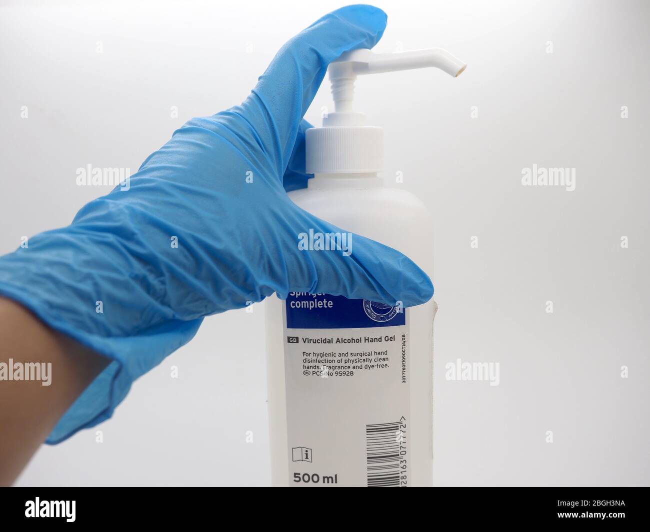 Una mano, indossando UN guanto monouso blu, raccogliendo UNA bottiglia di gel igienizzante, Londra, Regno Unito Foto Stock