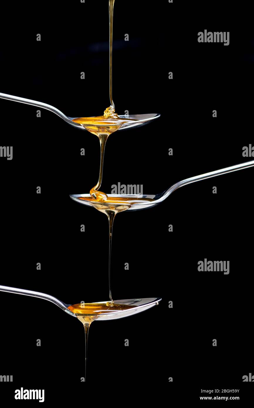 miele fresco che si versa su tre cucchiai Foto Stock