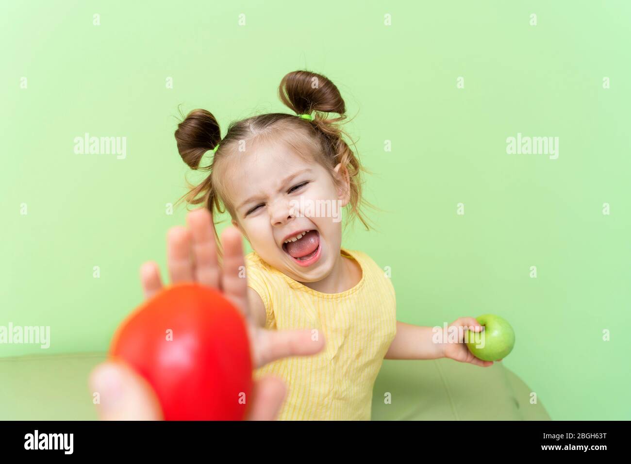 una bambina di 4-5 anni tiene in mano una mela, l'altra mano si estendeva al pomodoro in un gesto negativo. il rifiuto di childre Foto Stock