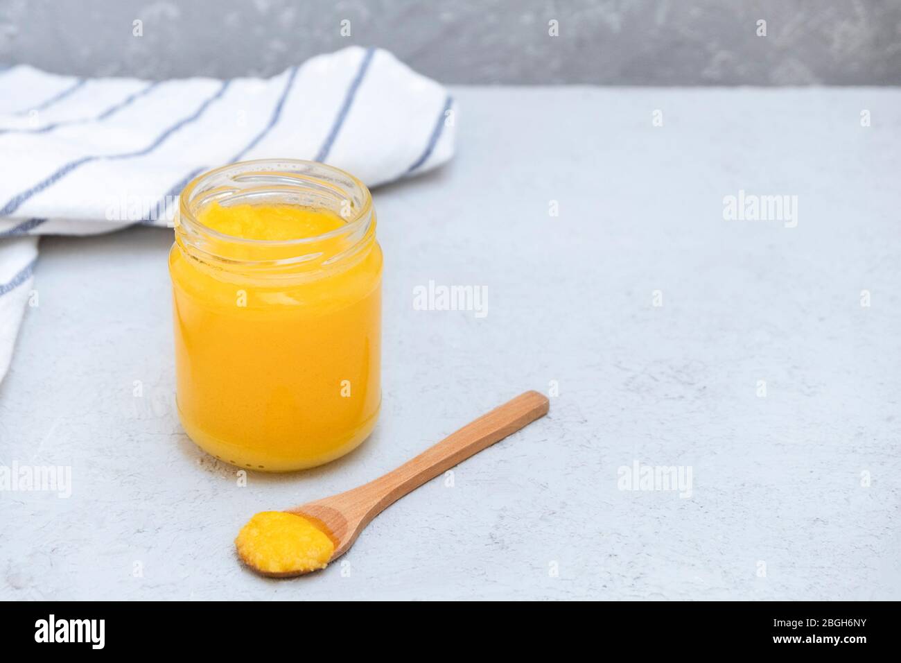 Desi ghee o burro chiarificato in un vaso e cucchiaio di legno su sfondo grigio neutro, spazio copia Foto Stock