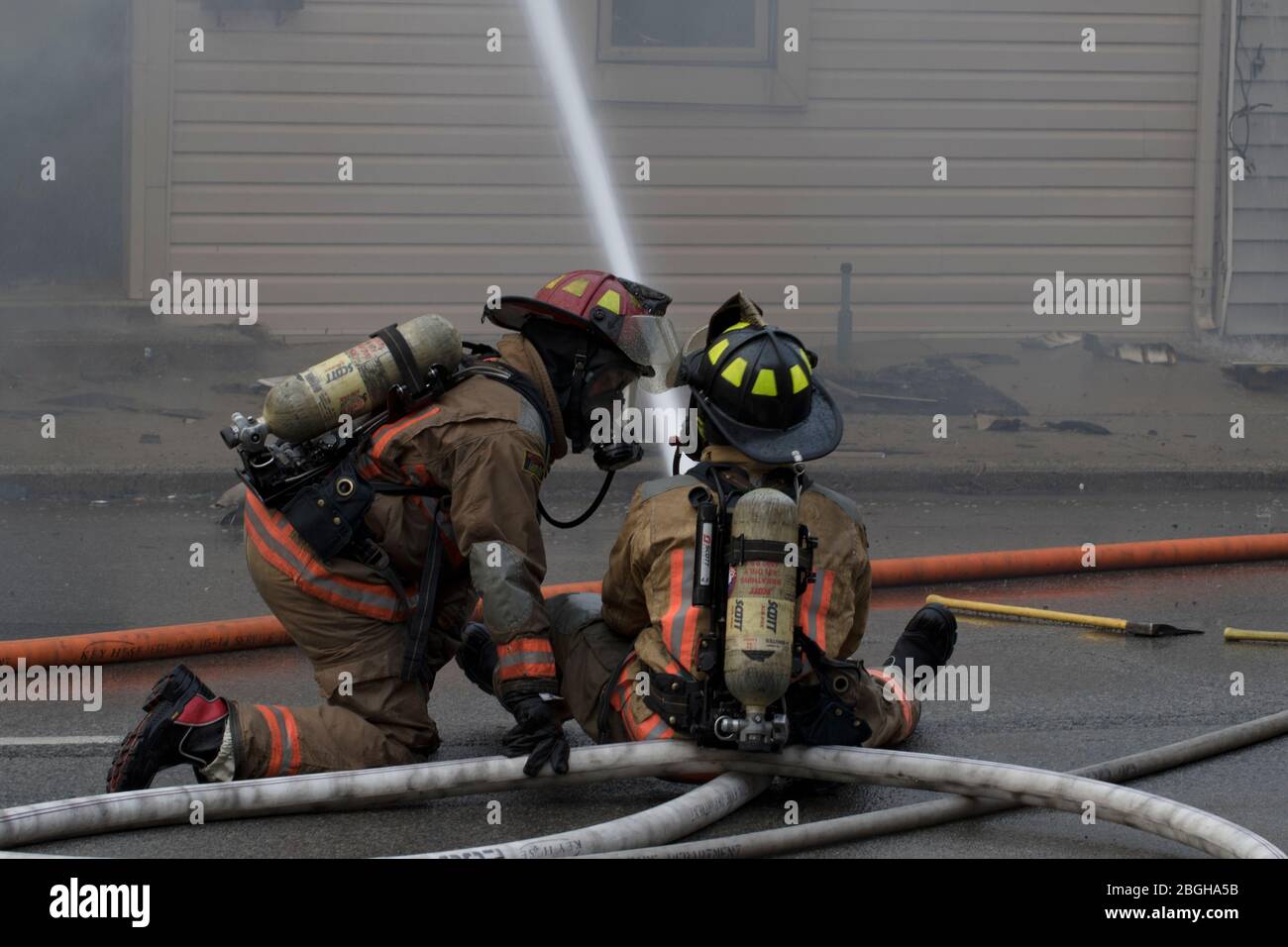 Due vigili del fuoco che tengono il tubo flessibile che mette fuori il fuoco della casa. Combattere il fuoco di grandi strutture. Foto Stock