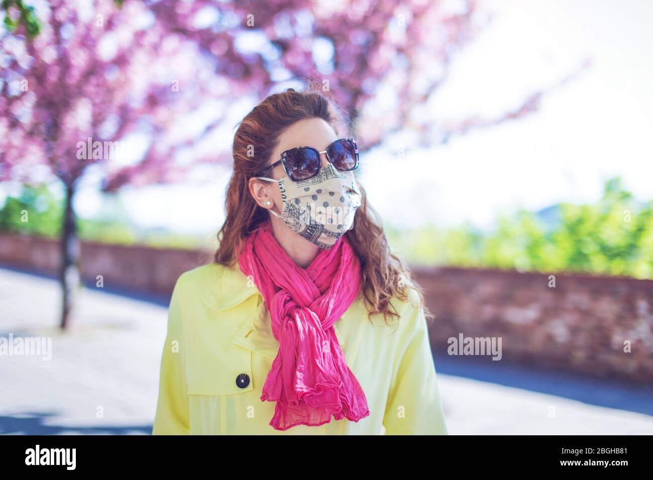 Giovane donna alla moda ritratto in maschera e occhiali da sole al parco durante sakura Foto Stock