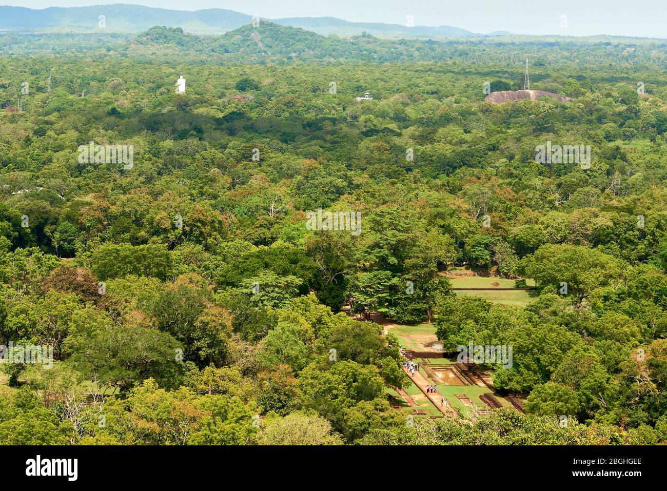 High angle shot di foresta a Sigiriya, Sri Lanka, con statua di Buddha in fondo e gruppi di turisti all'interno Sigiriya Rock Archeological S. Foto Stock