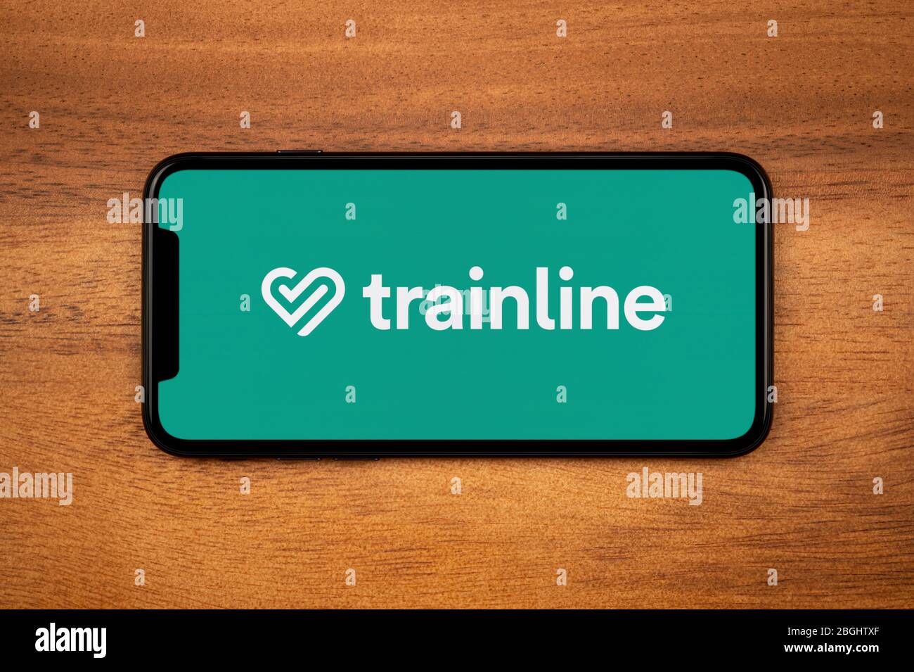 Uno smartphone con il logo Trainline è appoggiato su un tavolo di legno (solo per uso editoriale). Foto Stock