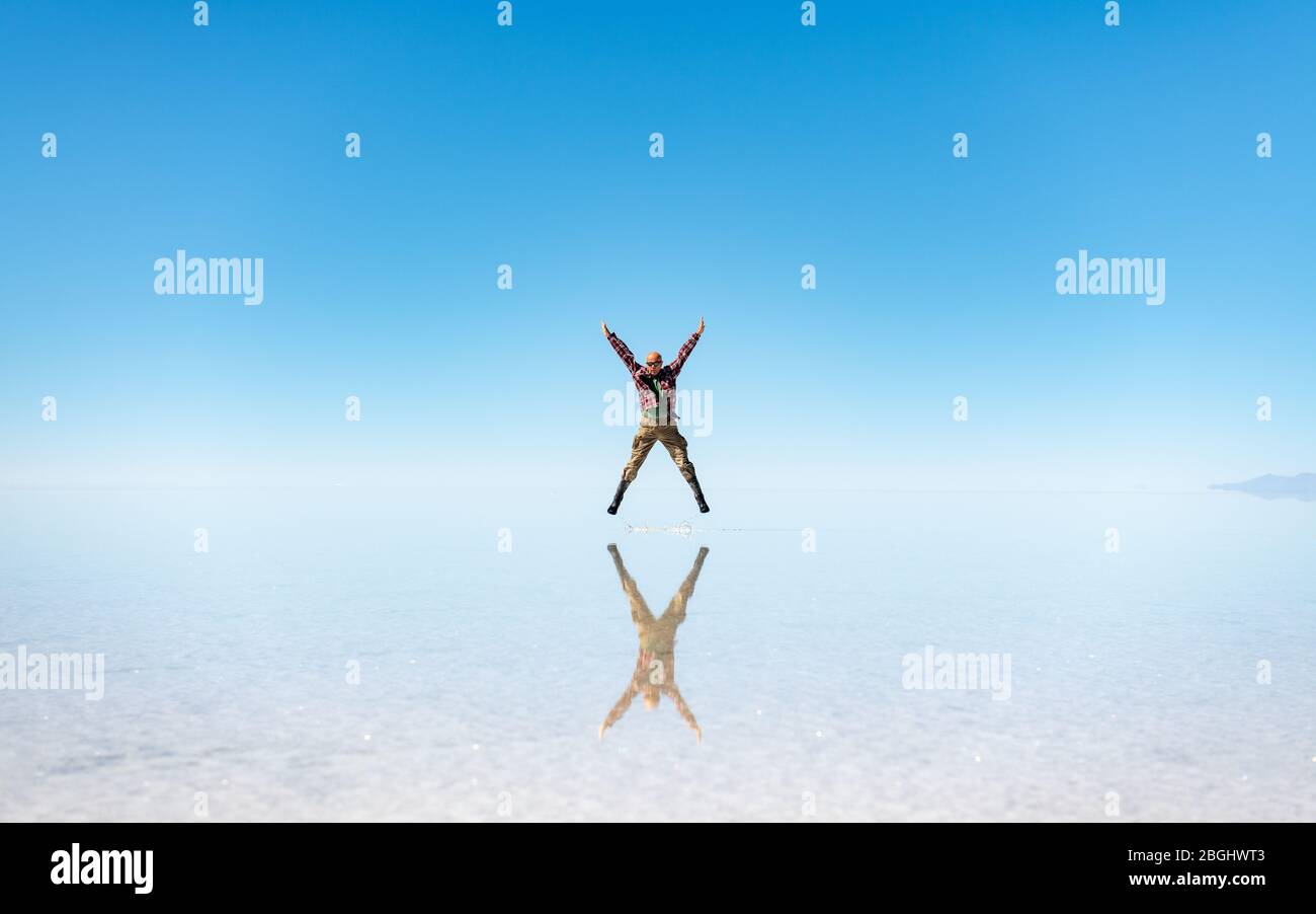 Uomo che salta a Salar de Uyuni, Salt Flats Uyuni, Bolivia sudoccidentale durante la stagione piovosa (bagnata) quando le saline sono allagate permettendo un riflesso specchio. Foto Stock