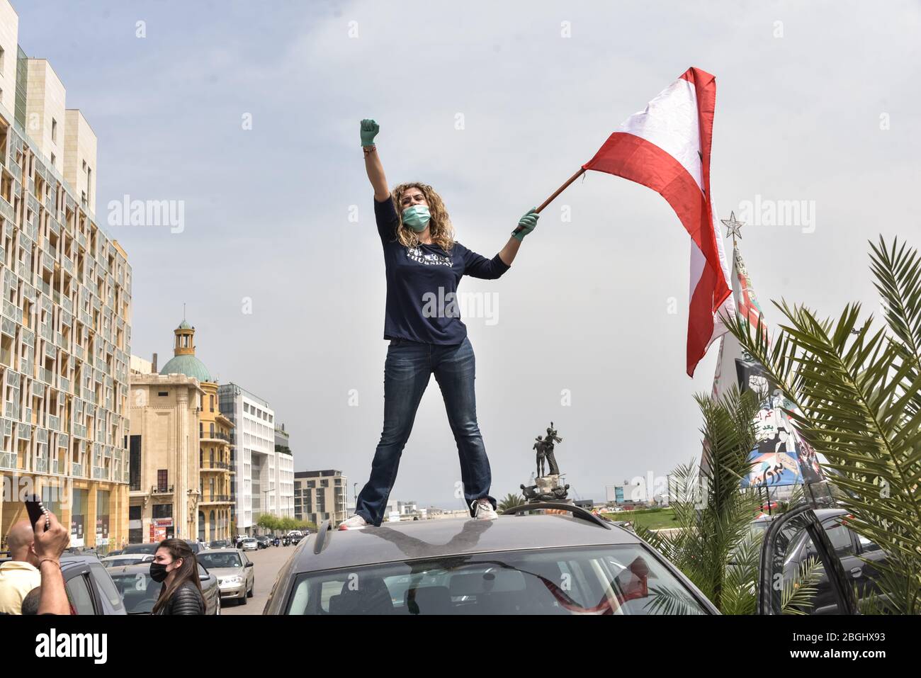 Beirut, Libano, 21 aprile 2020. Una donna alza il pugno in imitazione unconcious della statua che famosa Piazza dei Martiri sta levandosi davanti mentre la gente ha formato un convoglio dopo le centinaia riunitesi nella piazza dei Martiri nelle loro automobili per protestare contro la corruzione del loro governo e la mancanza di fornire i servizi adeguati o di gestire l'economico crollo del paese finanziariamente in difficoltà. Elizabeth Fitt Credit: Elizabeth Fitt/Alamy Live News Foto Stock