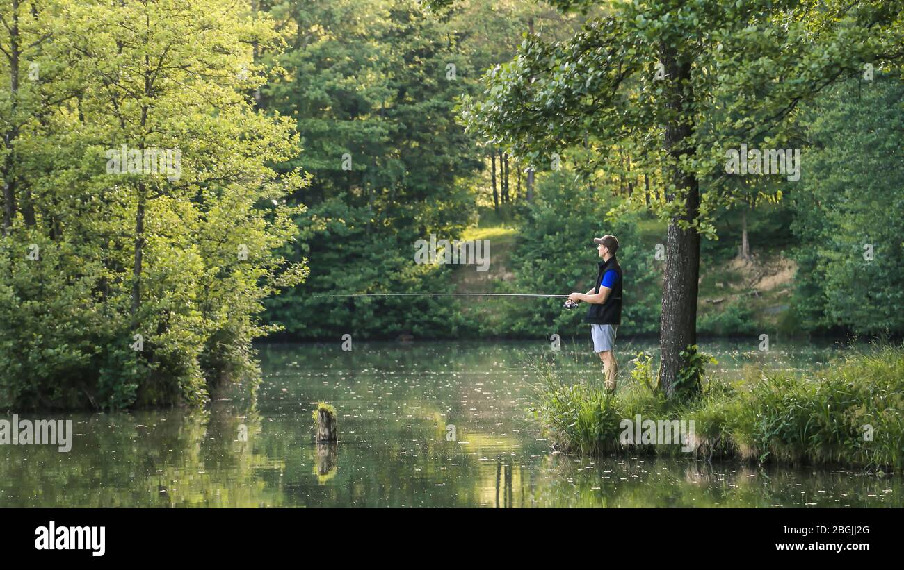 Uomo che pesca nel verde della natura selvaggia con la foresta lussureggiante in una giornata estiva soleggiata al tramonto. Foto Stock