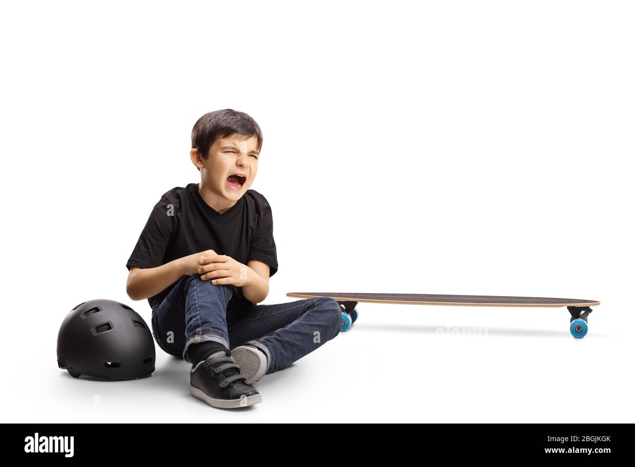 Bambino seduto sul pavimento piangendo e tenendo male il ginocchio da uno skateboard isolato su sfondo bianco Foto Stock