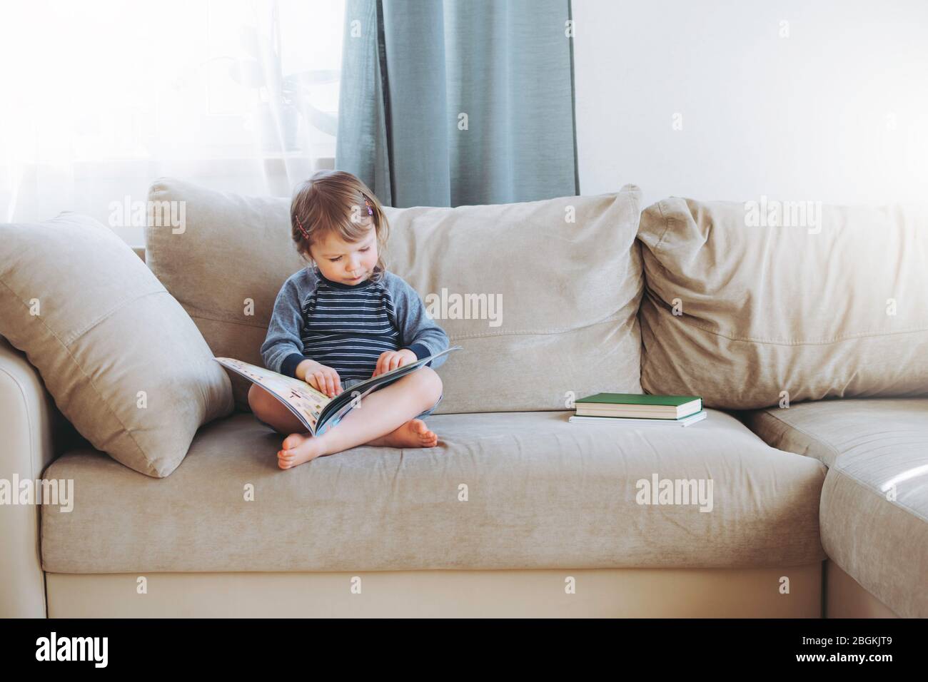 Bambina che legge un libro a casa sul divano. Formazione a distanza. Detox digitale. Foto Stock