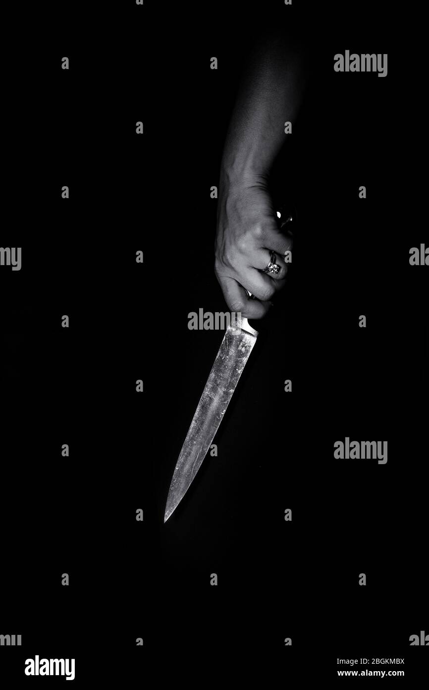 Donna che tiene un coltello grande in mano contro un fondo nero, concetto di omicidio, crimine, violenza, mistero, bianco e nero Foto Stock