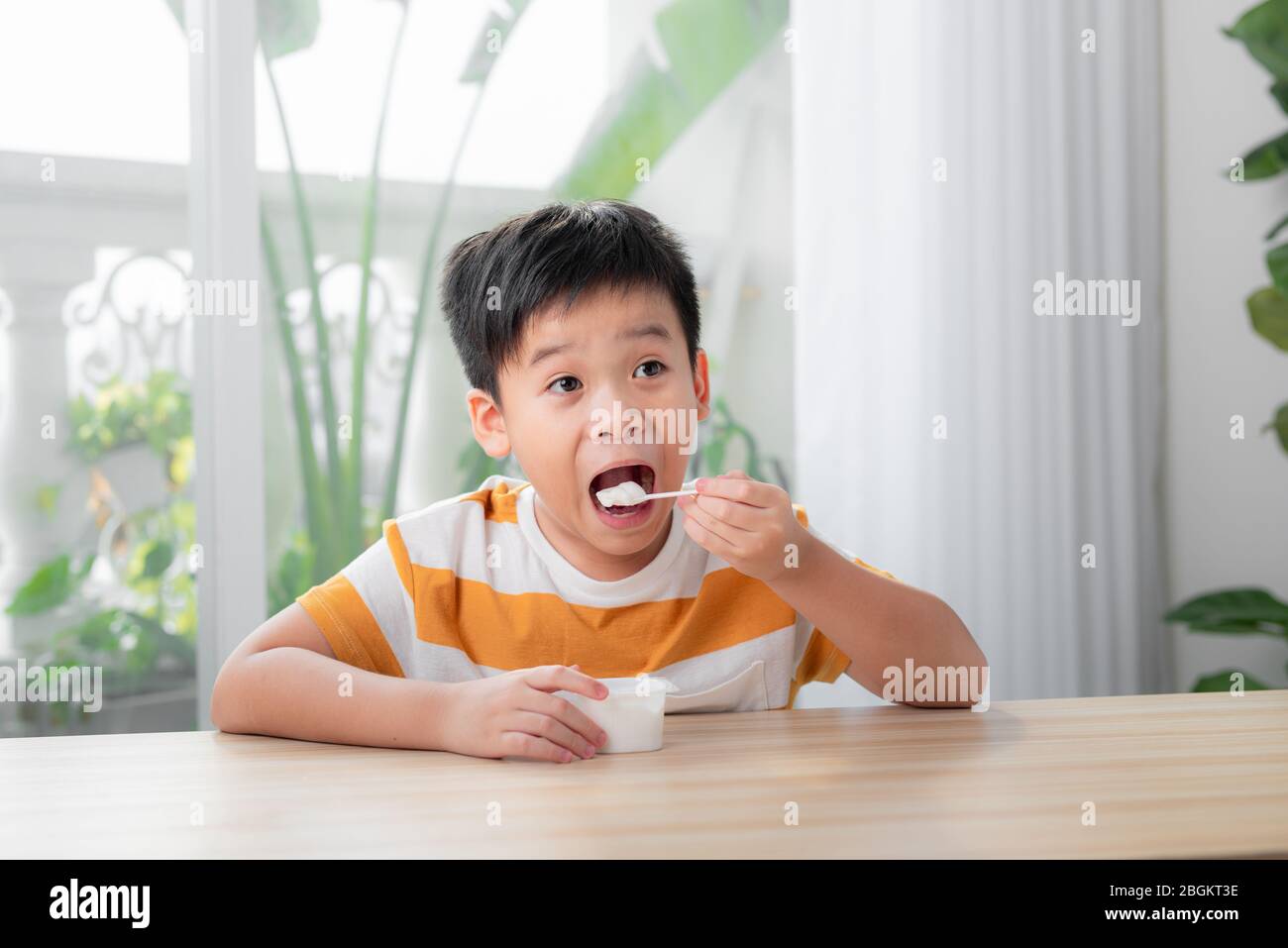 Ritratto di sorridente ragazzino mangiare delizioso yogurt Foto Stock