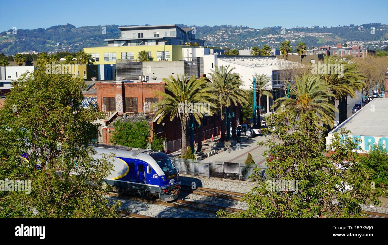Treno passeggeri Amtrak che passa attraverso Emeryville. Vista del Warehouse Lofts Emeryville e delle Oakland Hills sullo sfondo con palme. CA, STATI UNITI Foto Stock
