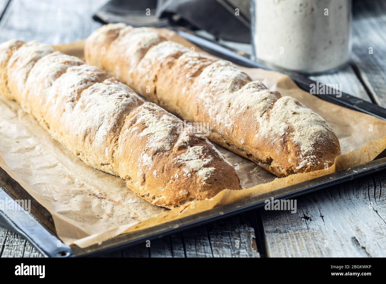 Baguette di pane di grano intero fresco su carta bagnata. Foto Stock