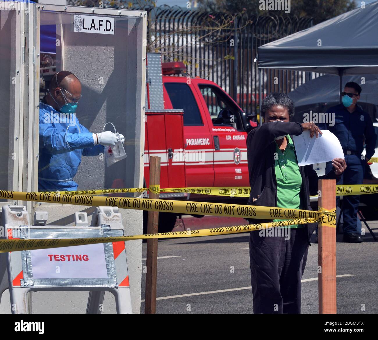 Una donna tossisce nel braccio prima di somministrare un kit di auto-test COVID-19 presso una stazione di test pop-up del Dipartimento DI LA Fire, dove i lavoratori in abiti Hazmat hanno consegnato tamponi di test ai senzatetto da dietro una finestra protettiva nella sezione Skid Row di Los Angeles martedì 21 aprile 2020. Altre quarantatre persone hanno dato prova di positivo per il coronavirus alla Union Rescue Mission, il più antico e più grande rifugio senza tetto di Los Angeles. L’improvviso picco dei casi arriva nonostante le precauzioni estreme che il riparo sta prendendo per prevenire un simile focolaio. Foto di Jim Ruymen/UPI Foto Stock
