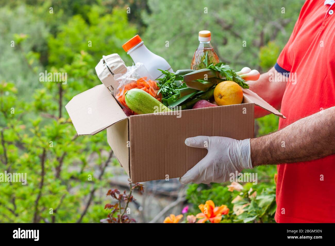 Consegna durante il concetto di quarantena o donazione di cibo. Uomo in guanti per uso medico che tiene la scatola con verdure e cibo. Foto Stock