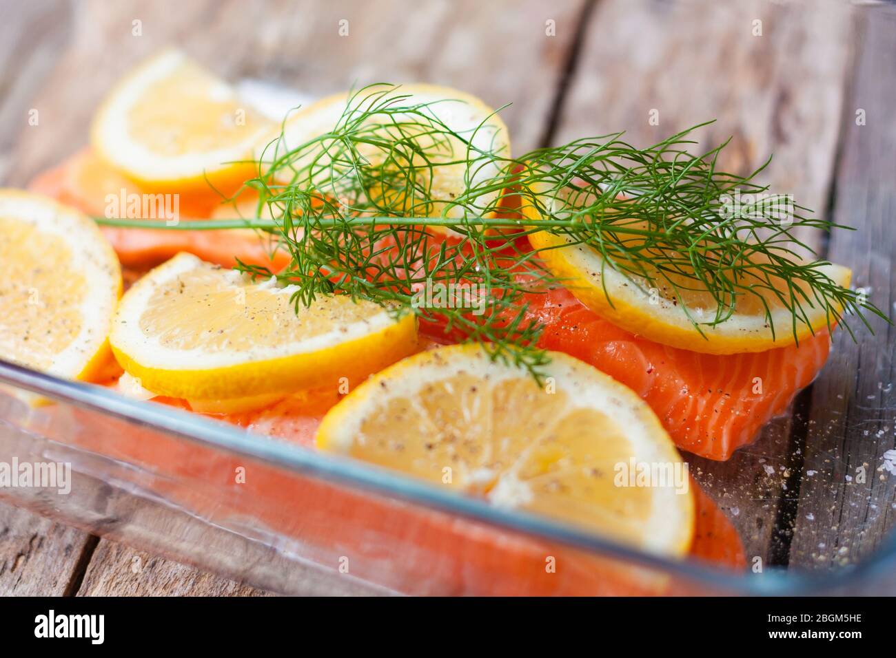Filetti di pesce rosso o salmone in vetro da forno su sfondo di legno. Pesce fresco, limone e aneto per cucinare gli ingredienti. Foto Stock