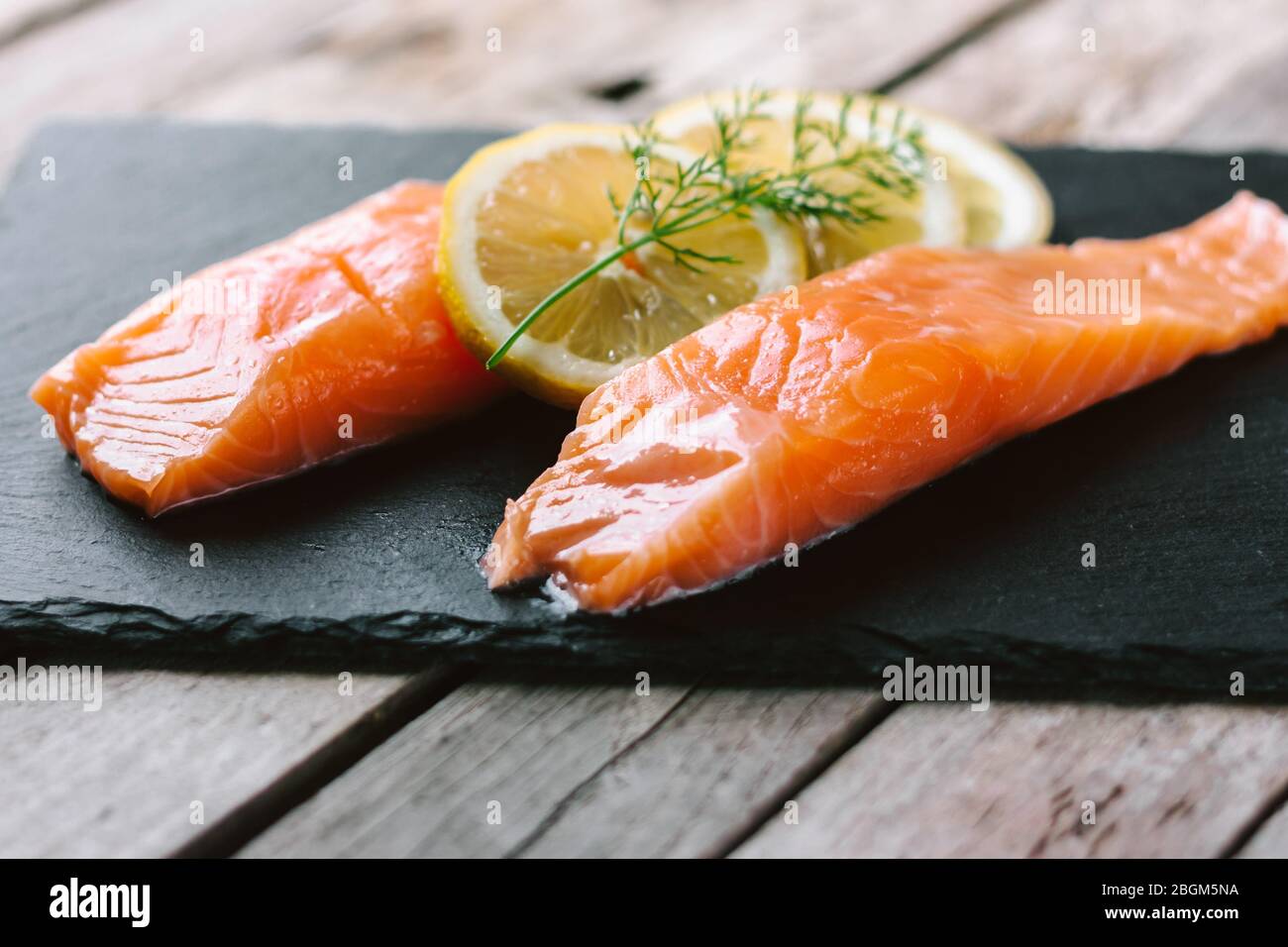 Filetti di pesce rosso o salmone su ardesia di pietra su tavola di legno. Pesce fresco, limone e aneto per cucinare gli ingredienti. Omega-3. Foto Stock