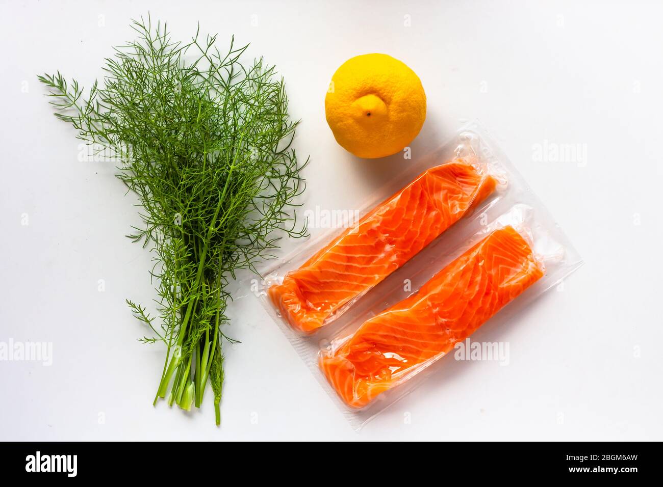 Filetti di pesce rosso o salmone in confezione sottovuoto su fondo bianco. Ingredienti per la cottura di pesce fresco, limone e aneto. Omega-3 Foto Stock