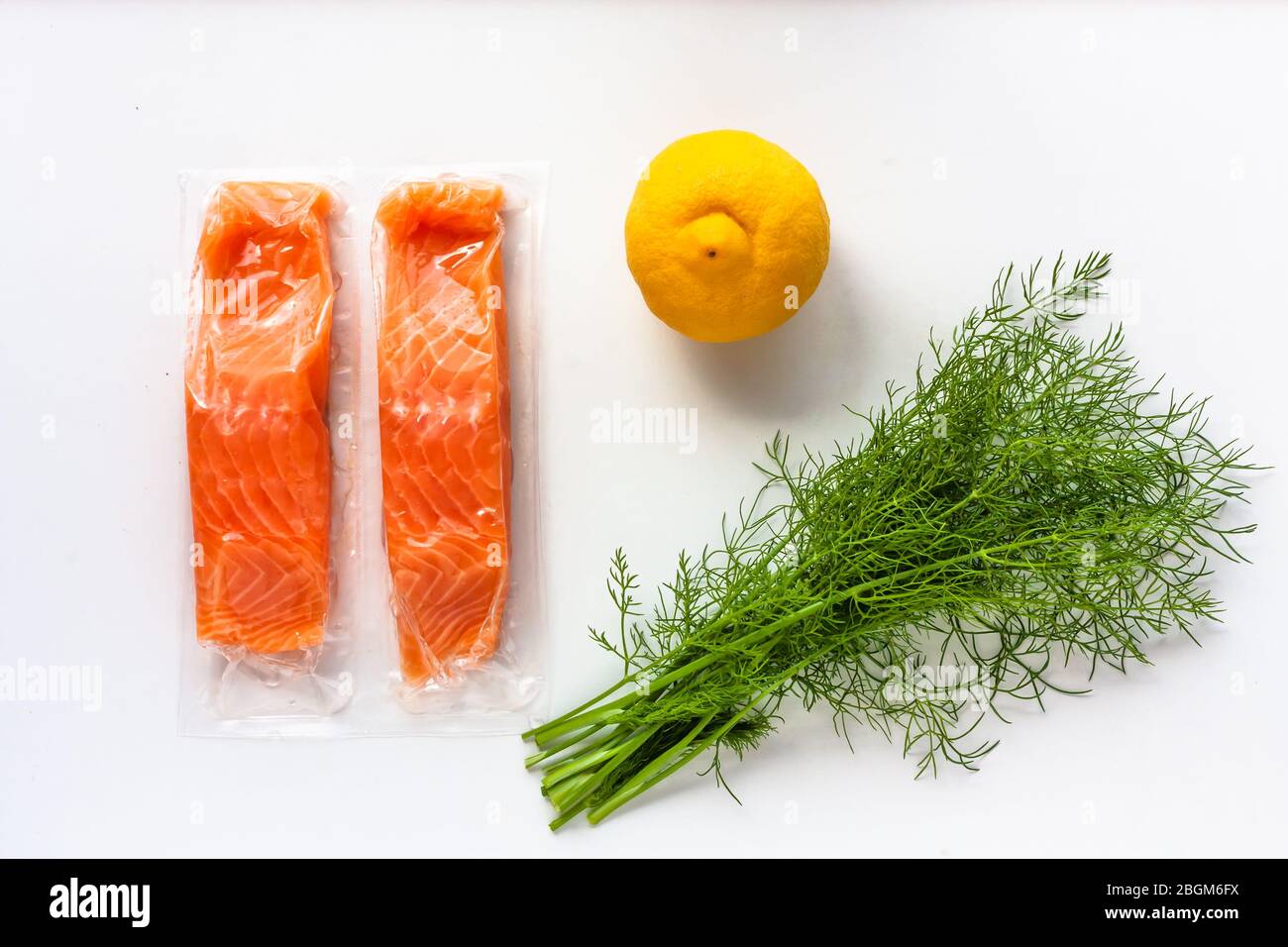 Filetti di pesce rosso o salmone in confezione sottovuoto su fondo bianco. Ingredienti per la cottura di pesce fresco, limone e aneto. Omega-3 Foto Stock