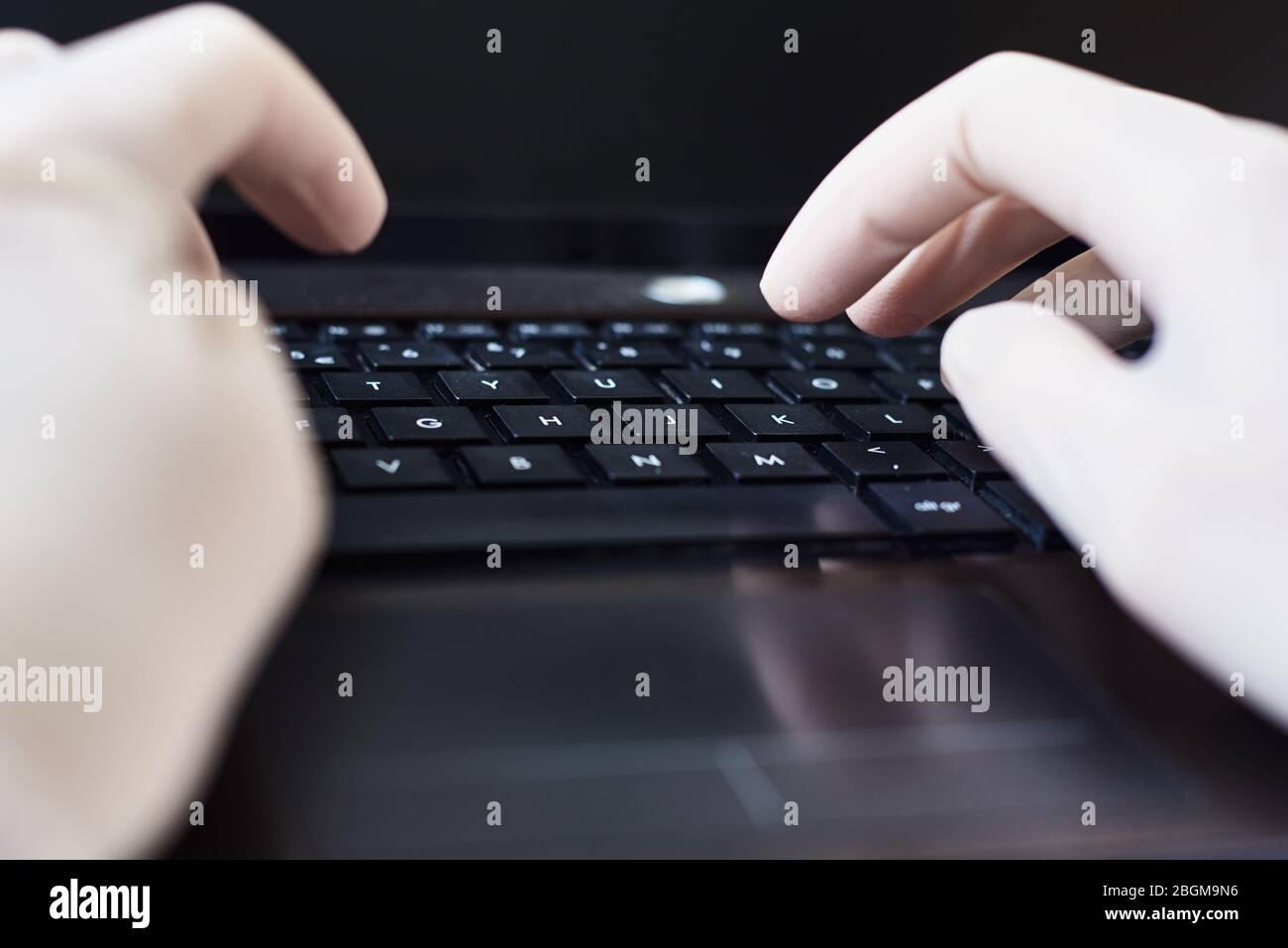 Mani nei guanti che digitano sulla tastiera del laptop. Concetto di protezione dai virus Foto Stock
