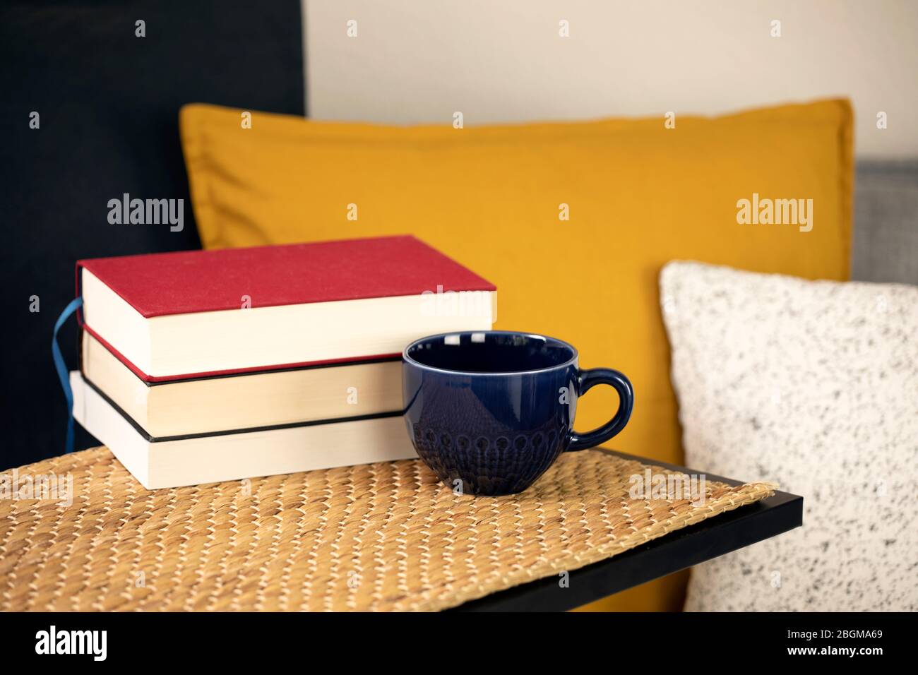 Molti libri con una tazza di caffè o tè sul tavolo con un comodo divano con cuscini e cuscini. Lettura di libri a casa, apprendimento. Attività ricreative Foto Stock