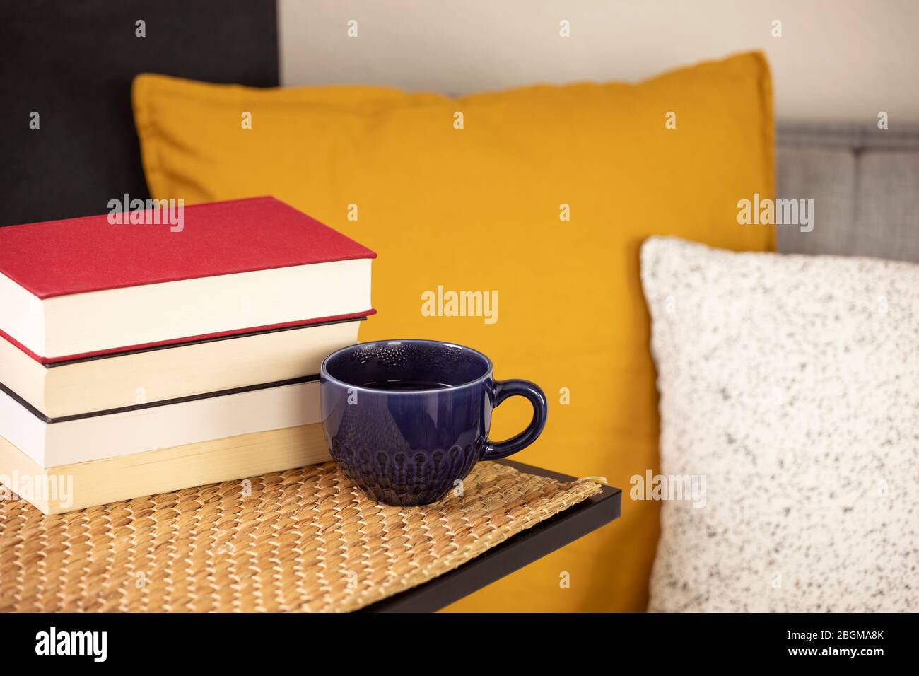 Tempo di lettura, pila di libri con tazza di caffè o tè sul tavolo con comodo divano con cuscini e cuscini. Lettura di libri a casa, apprendimento. Tempo libero Foto Stock