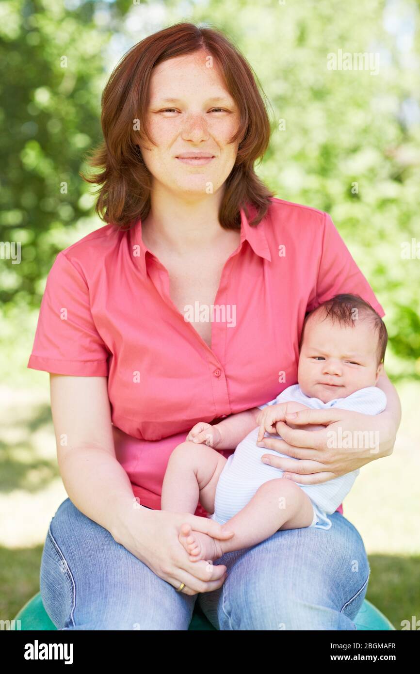 Glückliche Mutter im Grünen mit ihrem Baby auf dem Schoß Foto Stock