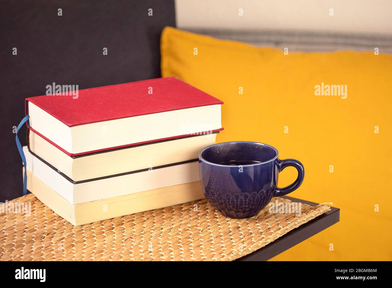 Molti libri con una tazza di caffè o tè sul tavolo con un comodo divano con cuscini e cuscini. Lettura di libri a casa, apprendimento. Attività ricreative Foto Stock