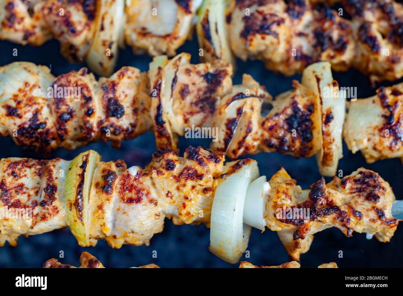 Gustoso barbecue arrosto primo piano. Kabobs di pollo fritto fatto in casa con cipolle cotte. Spiedini di carne di pollo grigliati su sfondo scuro. Foto Stock