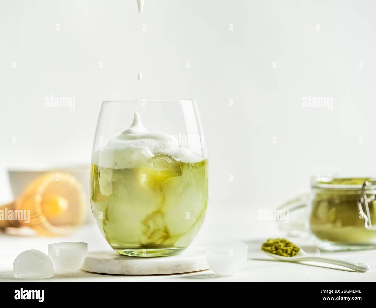 Tè Matcha latte ghiacciato con panna montata in bicchiere e ingredienti su sfondo di marmo bianco. Spazio di copia per txt o design Foto Stock
