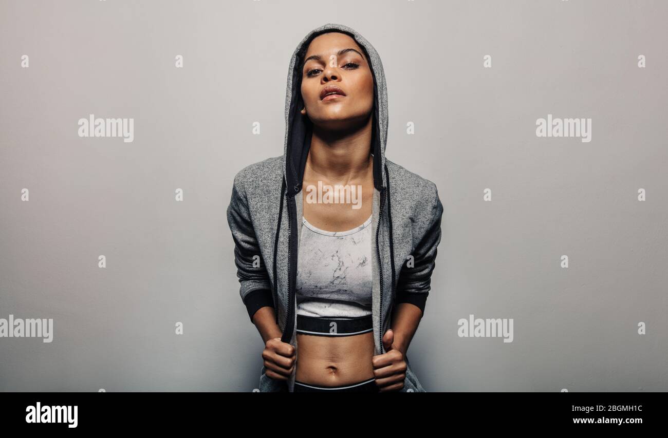 Donna che indossa una felpa con cappuccio e una tuta sportiva. Modello fitness femminile in posa in abbigliamento sportivo su sfondo grigio. Foto Stock